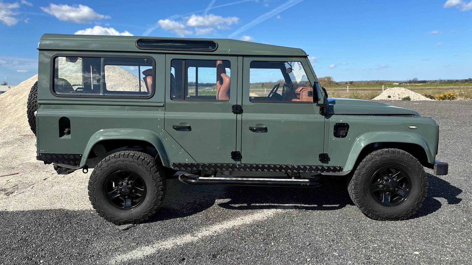 Side on view of Land Rover Defender 110 on an industrial park with a sunny blue sky in the background.