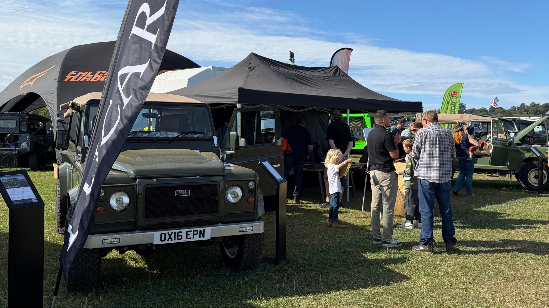 Land Rover Defender 90 with LUCARI branded flag at our show stand at the LRO Show at Belvoir Castle, visitors browsing nearby stalls in the background.