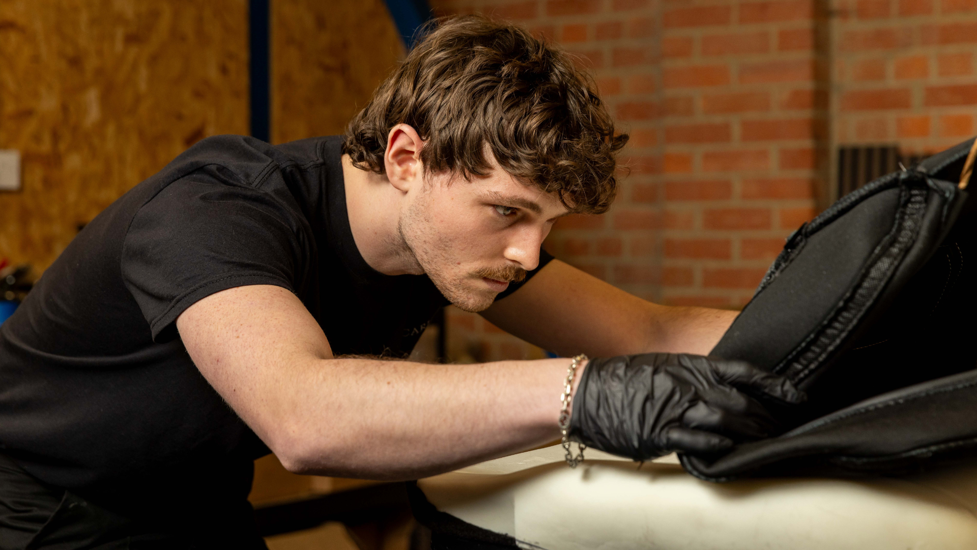 Close-up of a LUCARI trimmer inspecting stitching on a black seat panel in the workshop.