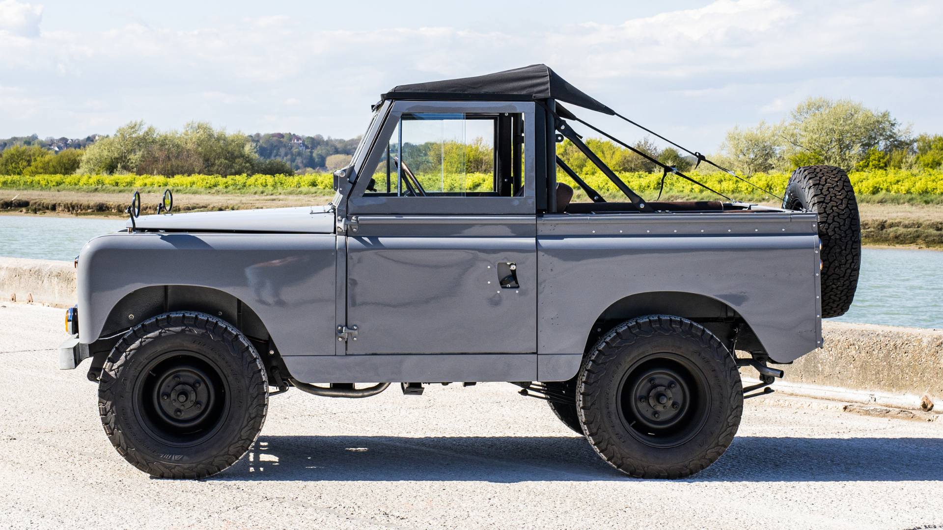 Grey Series soft top parked beside water, side profile showing black steel wheels and matt black bikini soft top hood.