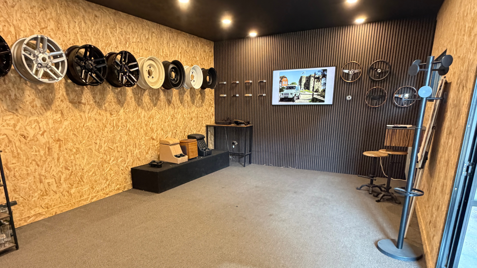 An empty looking LUCARI showroom display wall with Defender wheels and steering wheels mounted alongside cubby boxes.