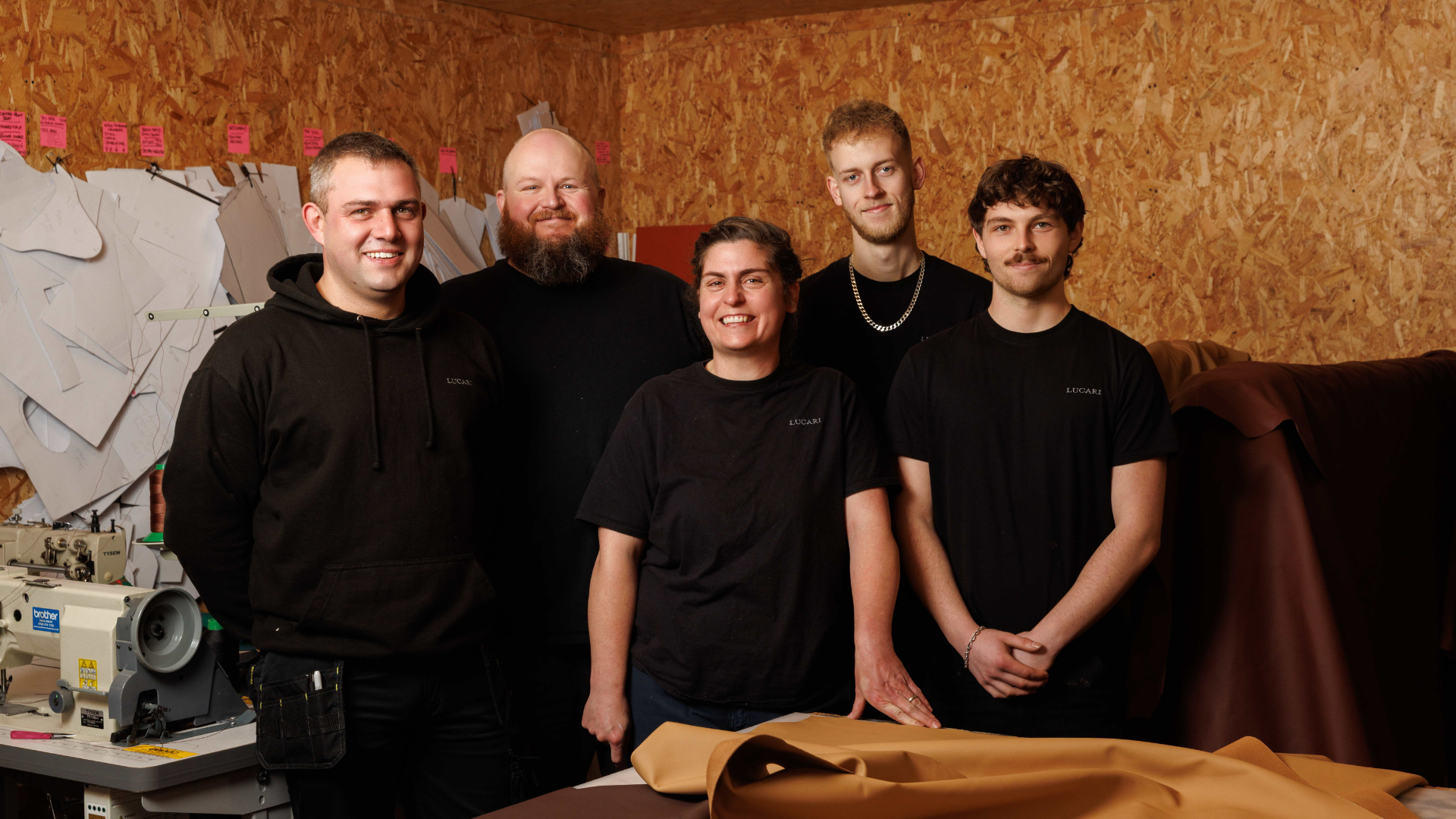 Five members of the LUCARI production team smiling together in the trim studio, surrounded by pattern templates and leather hides.