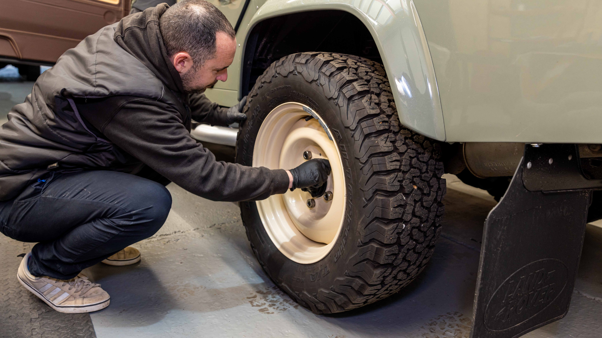 Technician fitting a cream steel wheel to a sage green Defender in the workshop.