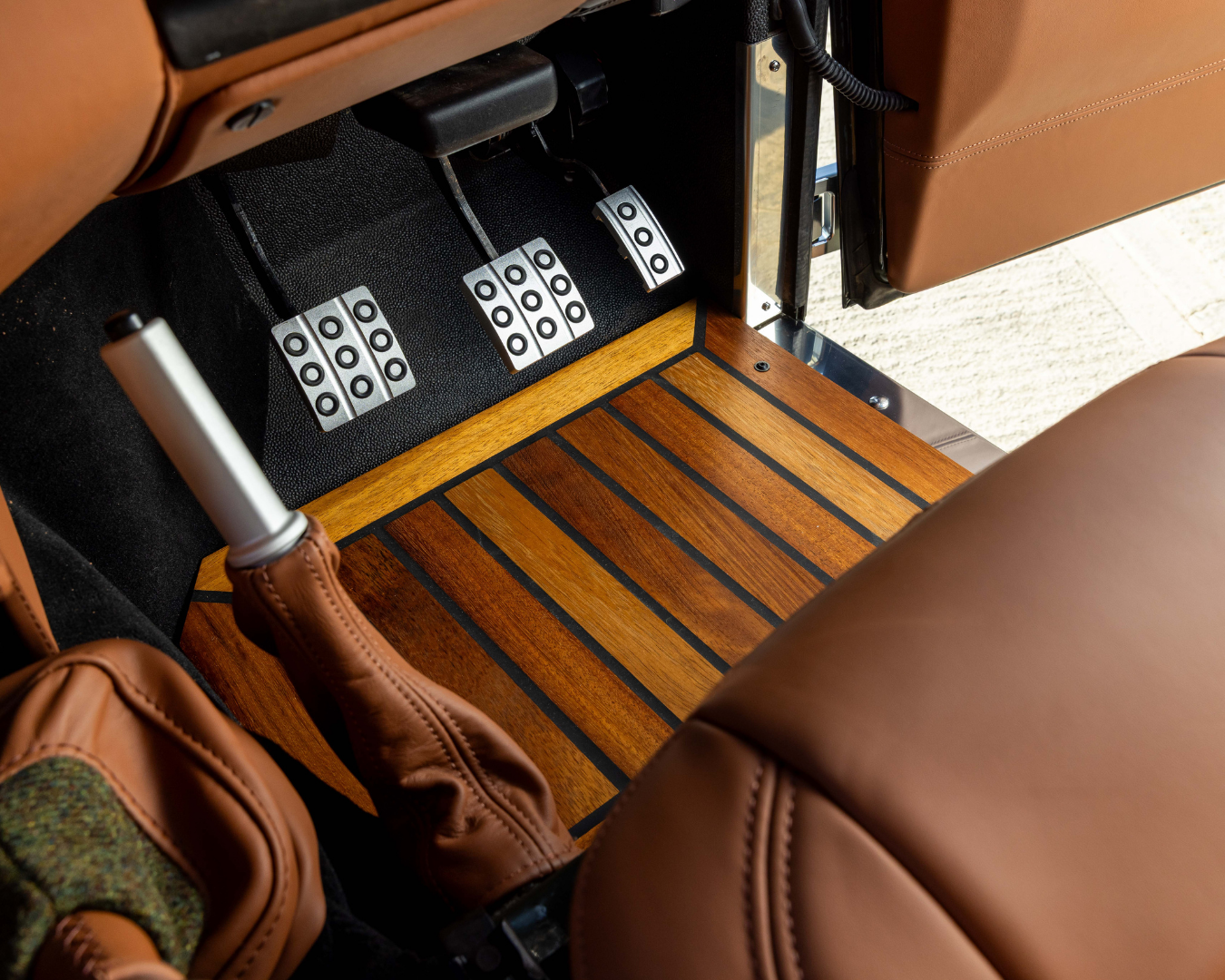 Iroko wood footwell flooring around the pedal box in a Land Rover Defender, finished with black inlay strips