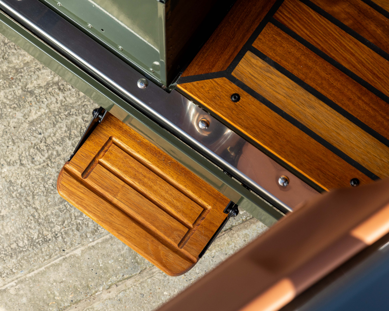 Fold-down Iroko wood step fitted to the rear chassis rail of a Land Rover Defender
