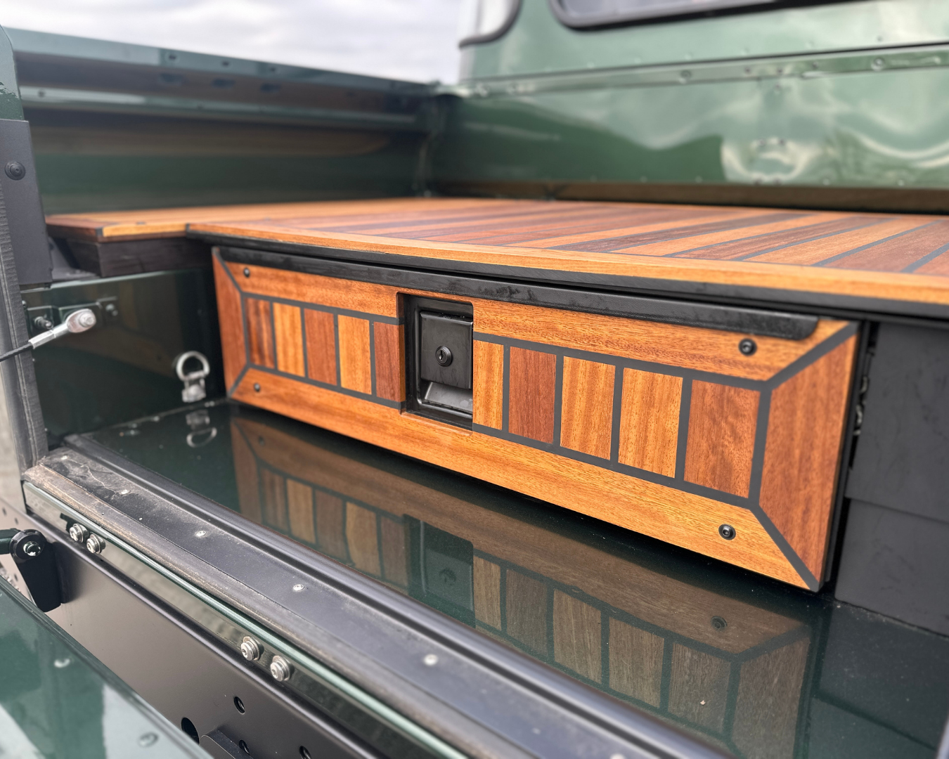 Iroko wood storage drawer with locking handle fitted into a Land Rover Defender load bay, deck flooring above