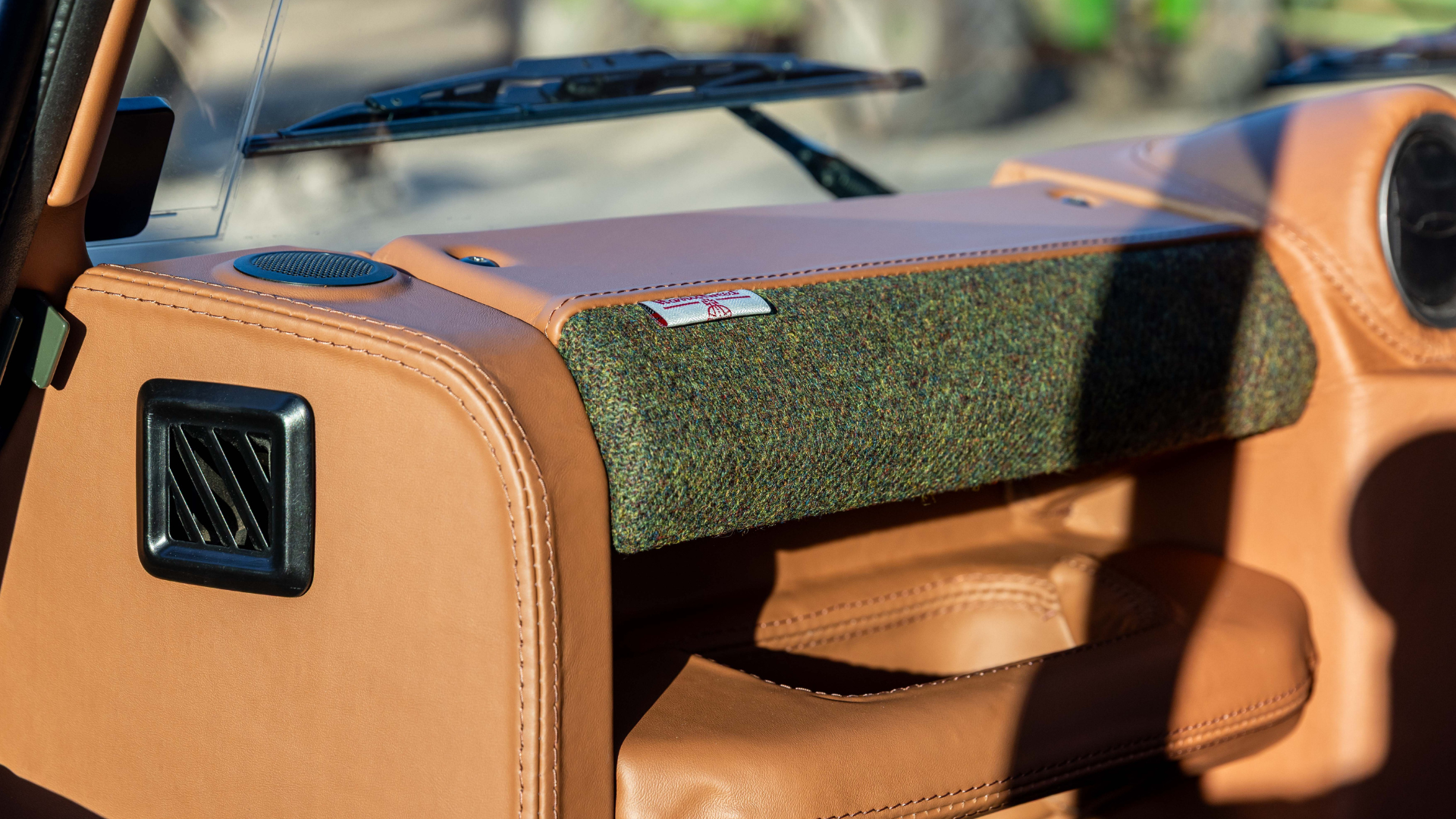 Detail shot of a Land Rover Defender dashboard finished in Tan leather with a Harris Tweed fabric panel, showing the woven Harris Tweed label.