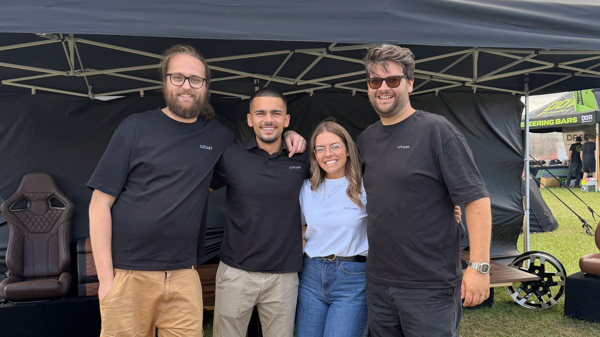 Four LUCARI team members in branded polo shirts smiling together at the show stand.