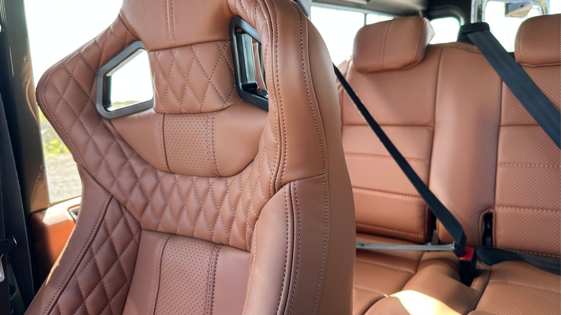 Rear interior of a Land Rover Defender 110 showing LUCARI Tan hex-quilted leather seats with integrated headrests, three-point seatbelts, and a consistent leather finish across all visible surfaces, photographed in natural light.