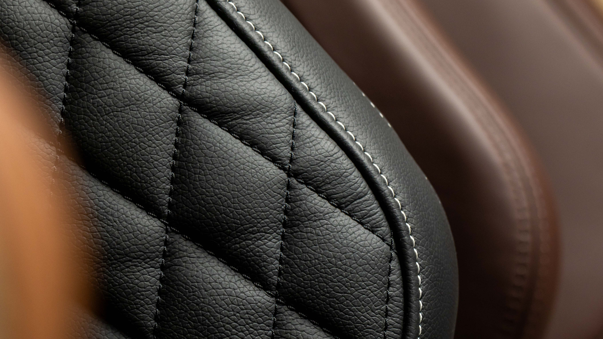 Close-up of quilted black leather stitching with contrast thread on a Defender seat.
