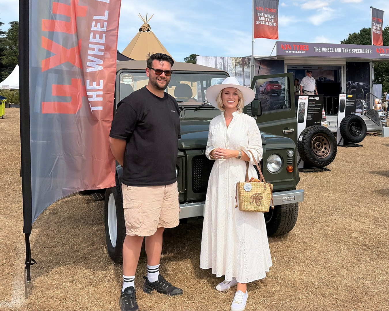 LUCARI team member and influencer The Little Green Defender standing in front of a  Defender 110 at The Game Fair on an event stand, the woman wearing a white dress and sun hat.