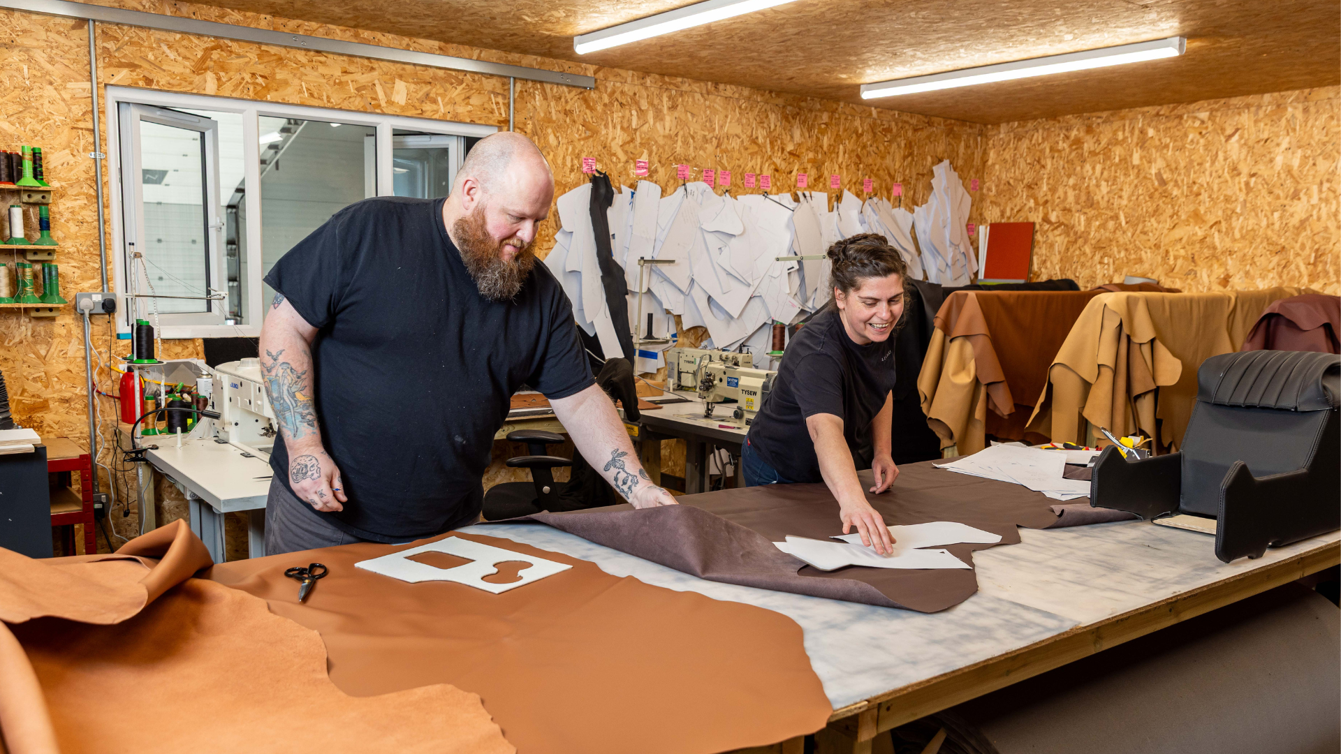 Two LUCARI team members laying out a pattern template on tan and chocolate leather hides at the cutting table.