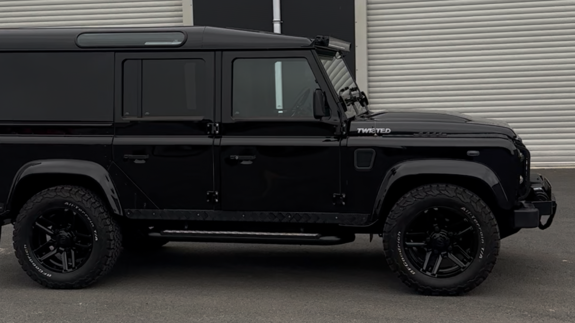 Side profile of a Santorini black Land Rover Defender 110 parked outside an industrial unit