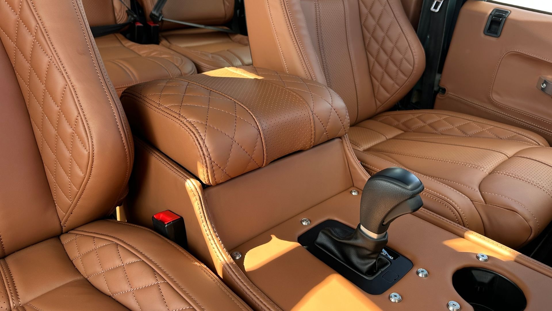 Close-up of the centre console area inside a Land Rover Defender 110, showing tan quilted leather seats and a matching auto cubby box.