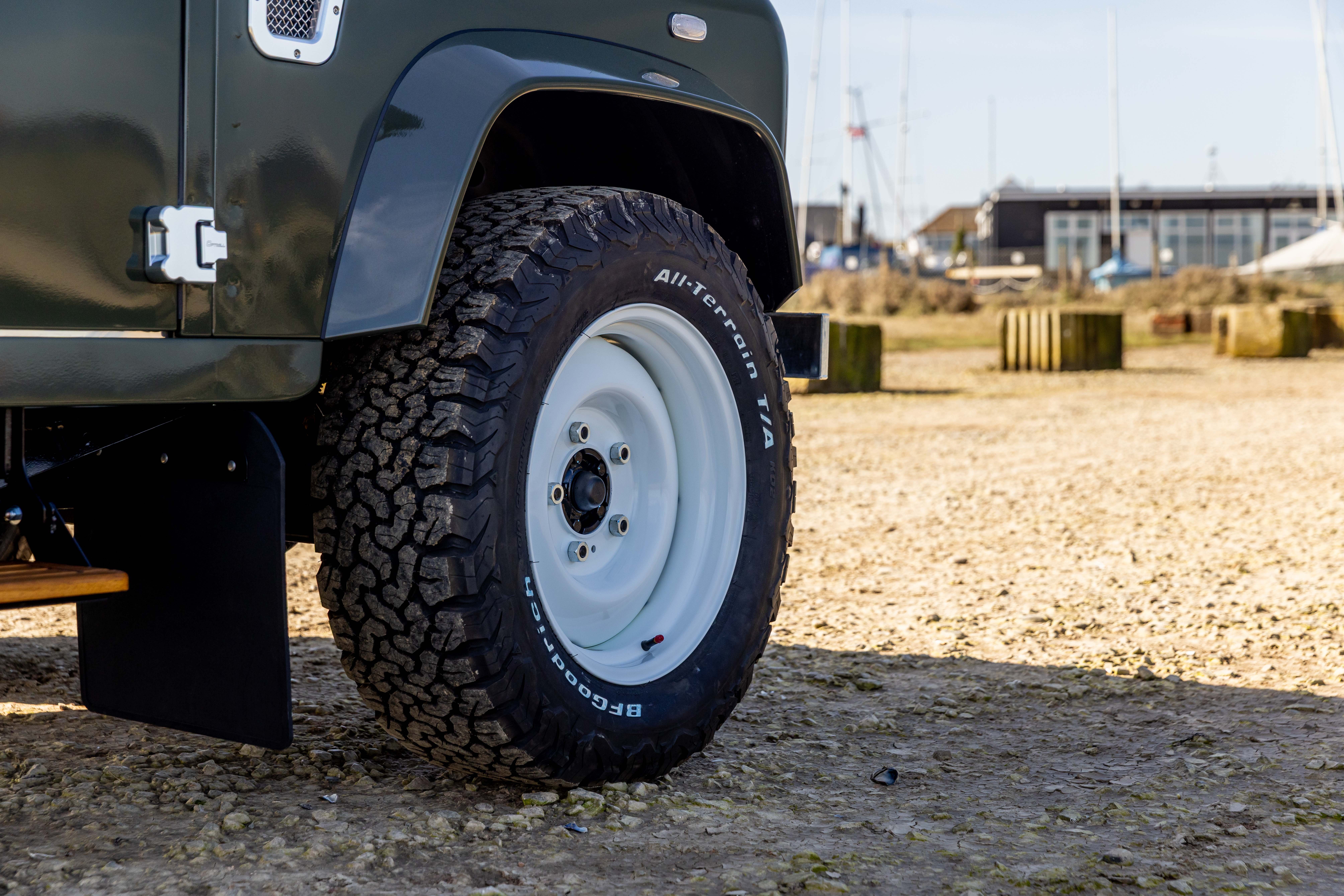 Low-angle rear view of an olive green Land Rover Defender 110 on gravel, fitted with a LUCARI White Steel 18" Wheel and BFGoodrich All-Terrain tyre