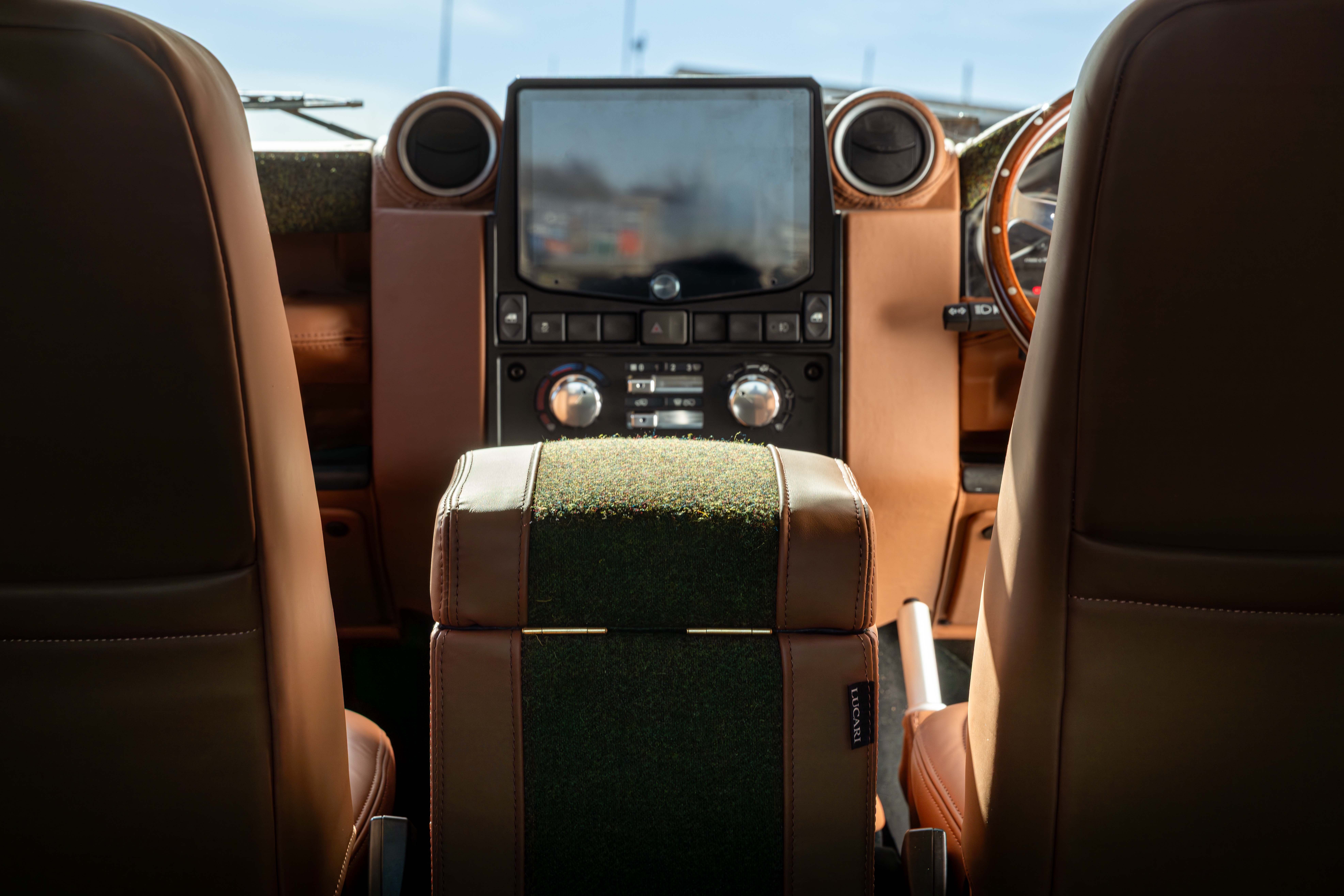 LUCARI-built Land Rover Defender centre console showing a Tan leather and Green Harris Tweed cubby box in the middle of front Tan leather seats and a entertainment system with chrome climate controls