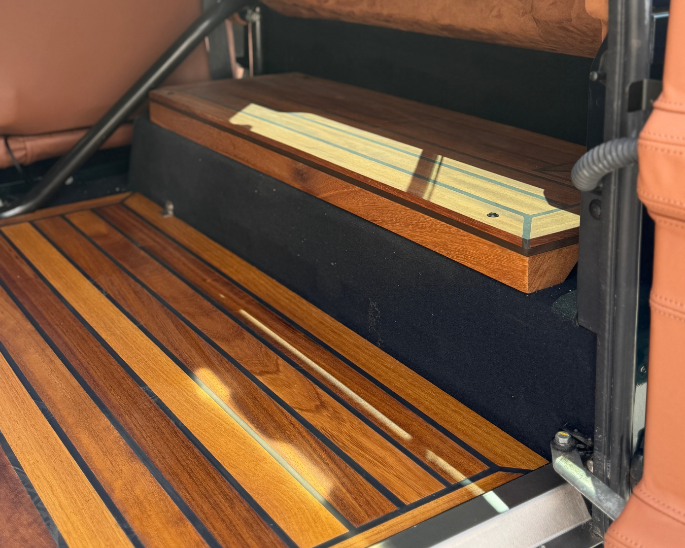 Iroko wood wheel arch top covers with inlay detailing beside deck-style flooring in a Land Rover Defender rear cabin