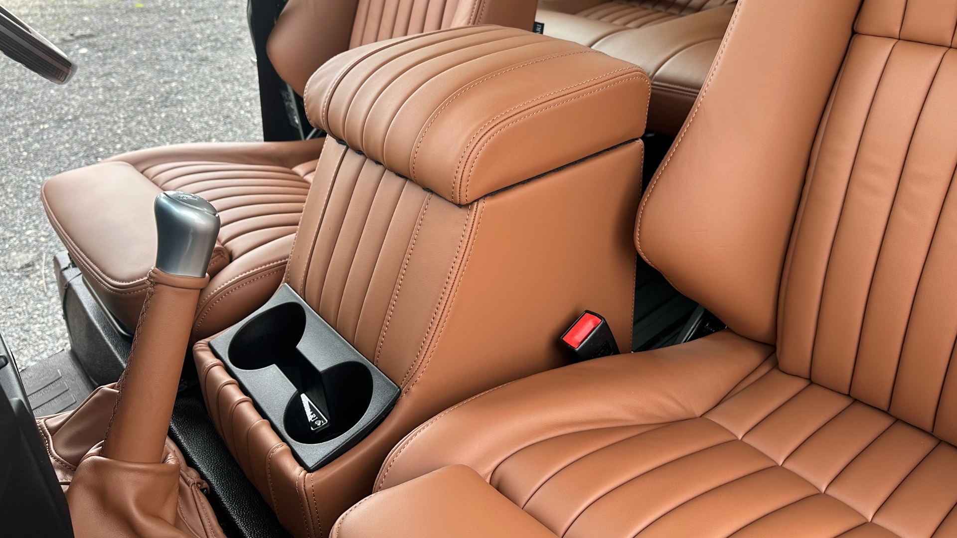 Defender centre cubby box in tan leather with integrated cup holders, viewed between the front seats.