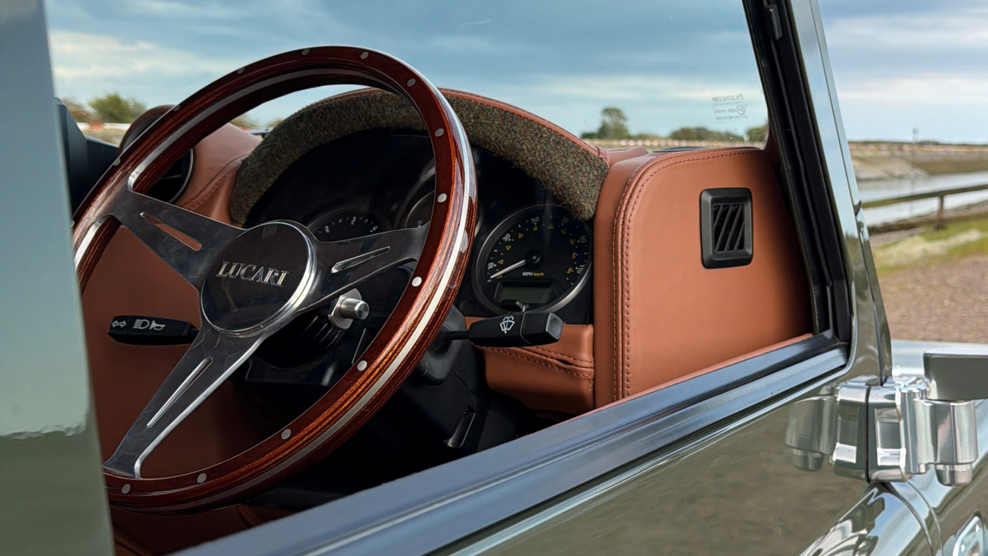Close-up of a LUCARI wooden dished steering wheel with Harris Tweed dash trim, viewed through the open driver's door.