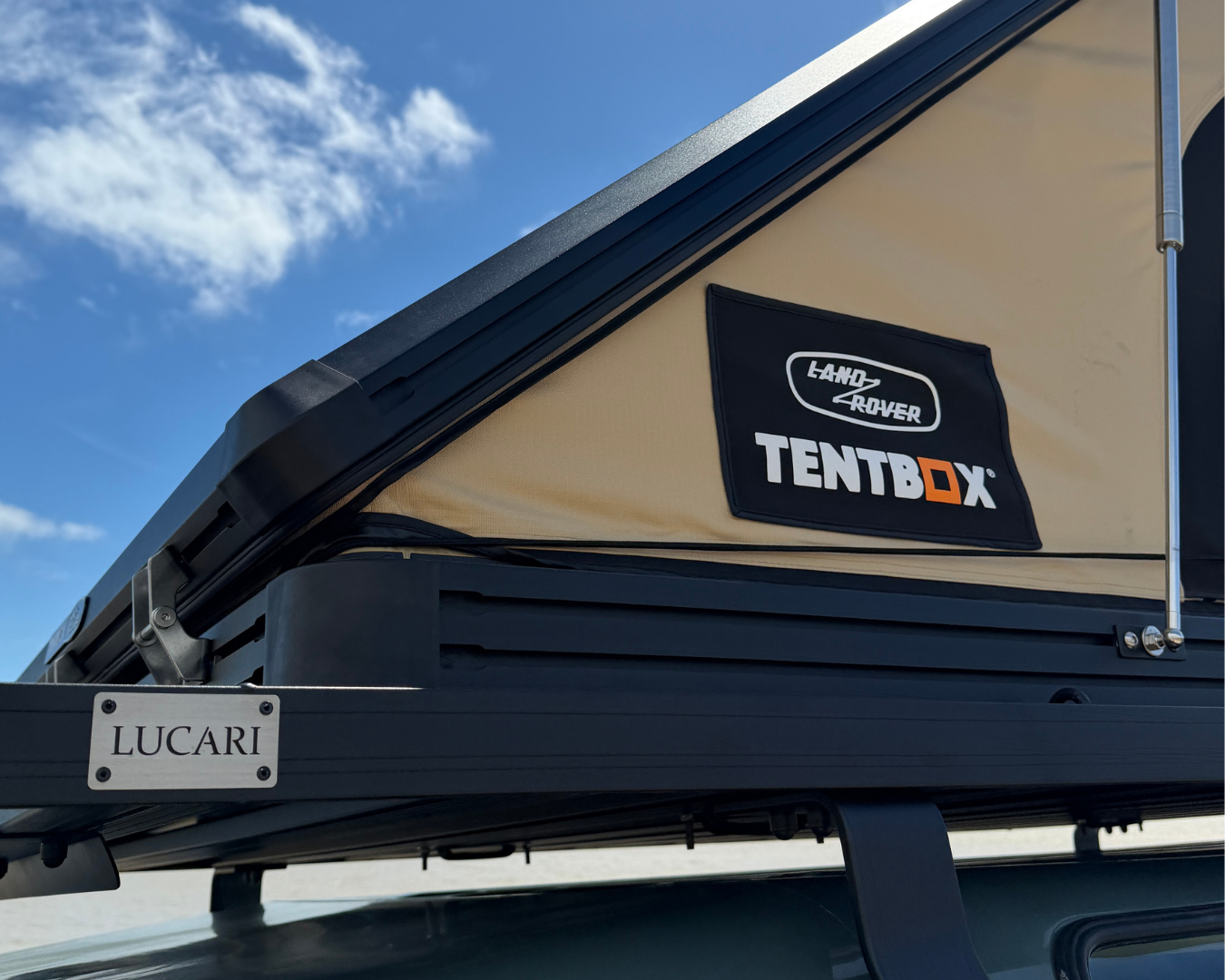 TentBox roof tent open mounted on a LUCARI Defender 110 Roof Rack against a blue sky