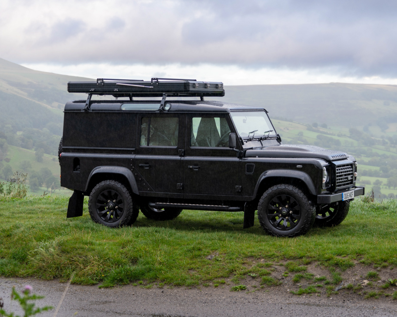 Black Land Rover Defender 110 with roof rack and TentBox Cargo, Land Rover edition, fitted and parked on hillside in wet conditions