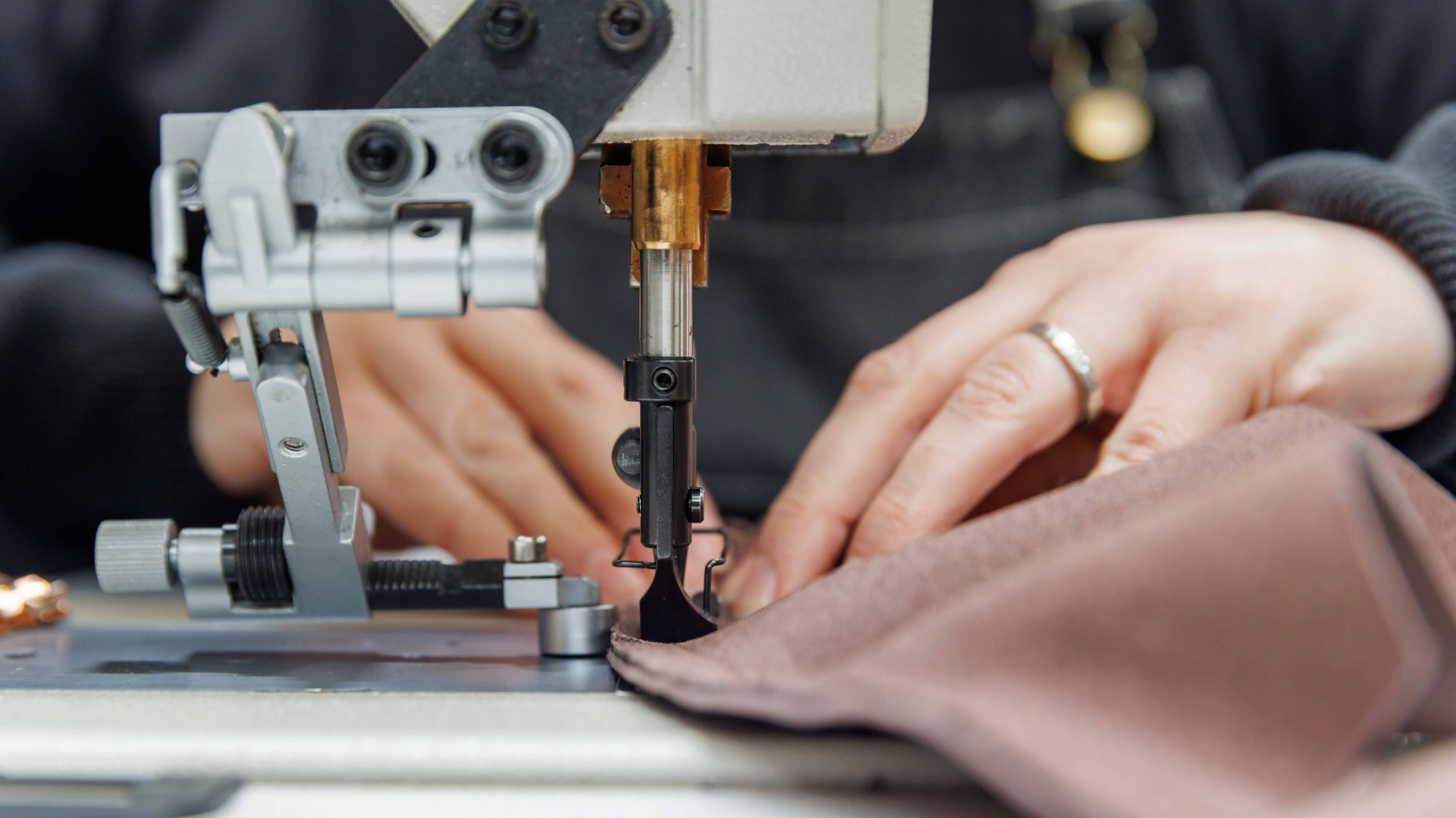 Close-up of hands guiding leather under a sewing machine needle in the LUCARI trim studio.